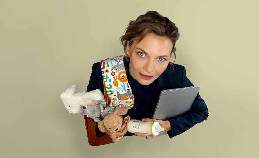 Women juggling laptop and baby bottle, stuffed toys and blanket.