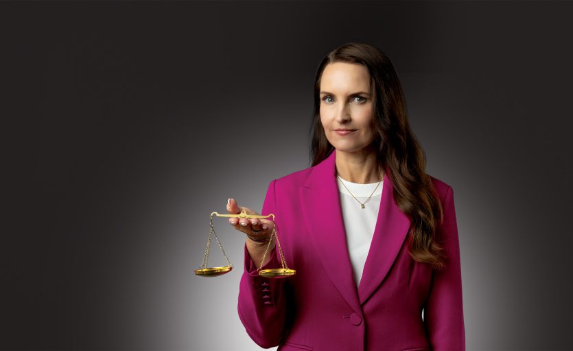 Woman in pink suit jacket balancing legal scale on her hand.