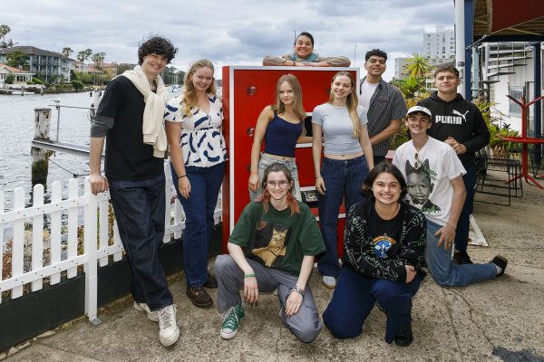 A group of students stand around a giant red E. There is water behind them.