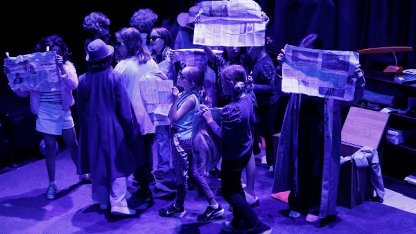 Students on a group, under blue lighting holding newspapers and other props