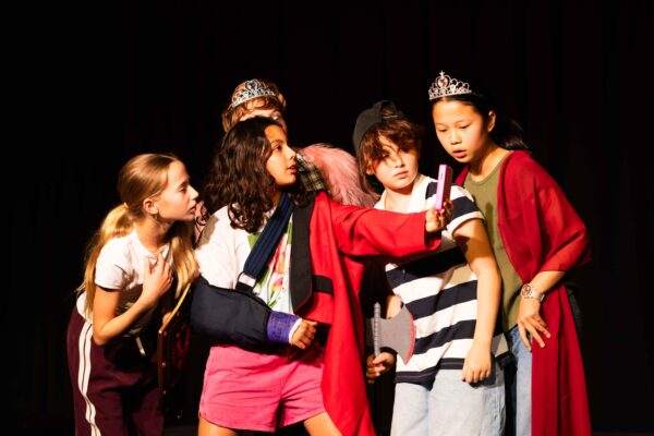 A group of students with colourful costume, look into a prop mobile phone.